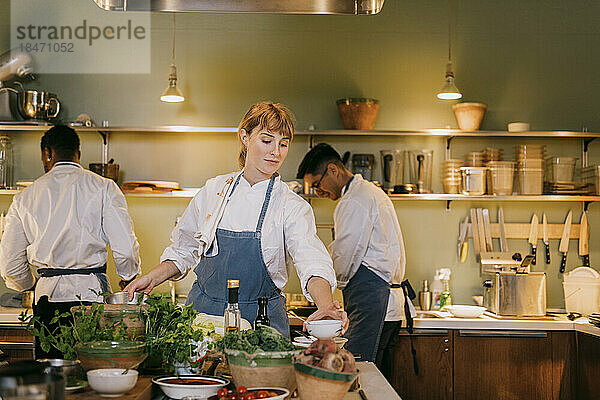 Junge Köchin bei der Zubereitung von Speisen mit Kollegen in einer Großküche