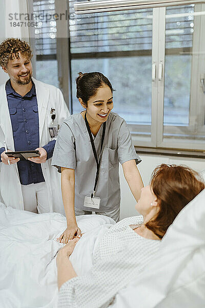 Lächelnde Krankenschwester im Gespräch mit einer älteren Patientin  die auf dem Bett eines Arztes im Krankenhaus liegt