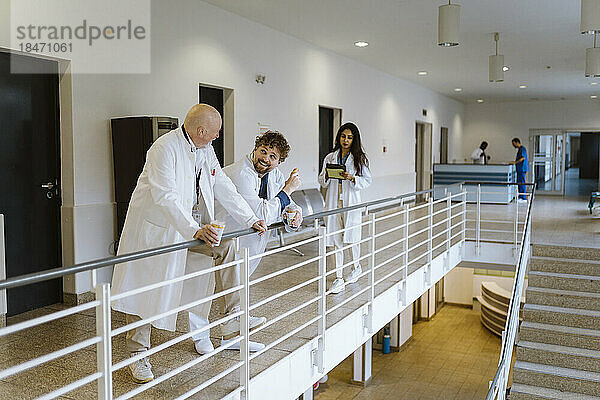 Lächelnde männliche Ärzte  die sich in der Kaffeepause mit einer weiblichen Kollegin auf dem Krankenhausflur unterhalten