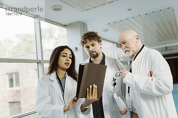 Ärztin diskutiert mit männlichen Kollegen auf dem Krankenhausflur über ein digitales Tablet