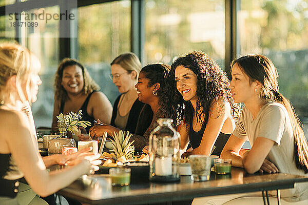 Fröhliche  gemischtrassige Freundinnen sitzen am Esstisch  während sie in einem Rückzugszentrum frühstücken