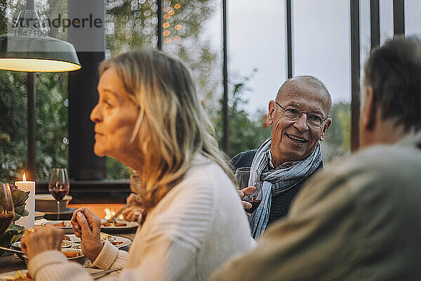 Lächelnder Mann im Ruhestand im Gespräch mit einem männlichen Freund bei einer Dinnerparty