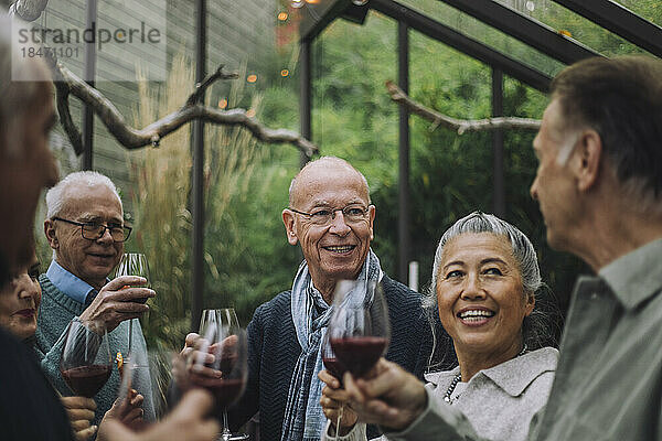Lächelnder älterer Mann im Gespräch mit männlichen und weiblichen Freunden im Ruhestand auf einer Party