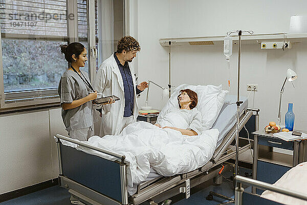 Mitarbeiter des Gesundheitswesens im Gespräch mit einer älteren Patientin  die auf einem Bett im Krankenhaus liegt