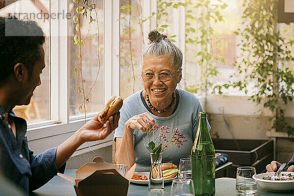 Glückliche ältere Frau genießt das Essen mit einem männlichen Freund  während sie im Restaurant sitzt