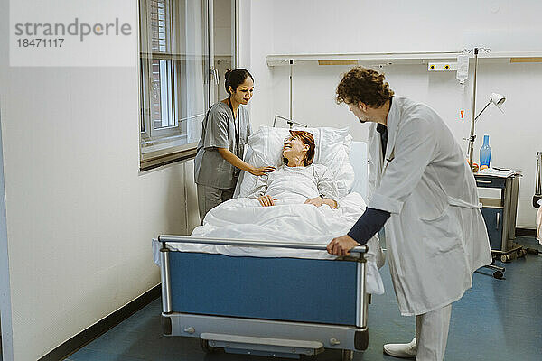 Lächelnde ältere Patientin auf dem Bett liegend  inmitten von Pflegepersonal im Krankenhaus