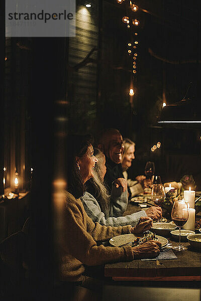 Männliche und weibliche ältere Freunde genießen ein gemeinsames Abendessen bei Kerzenschein während einer Party in der Nacht