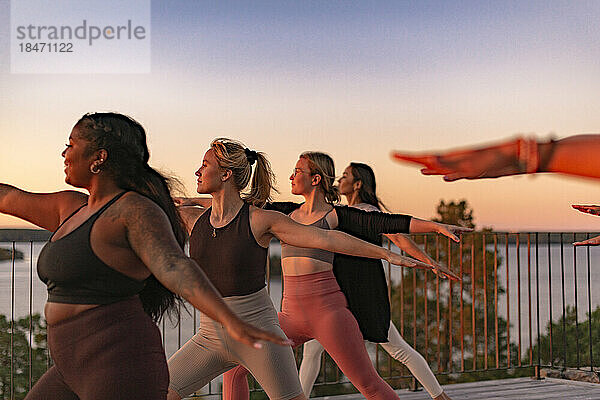 Freundinnen beim Yoga auf der Terrasse bei Sonnenuntergang