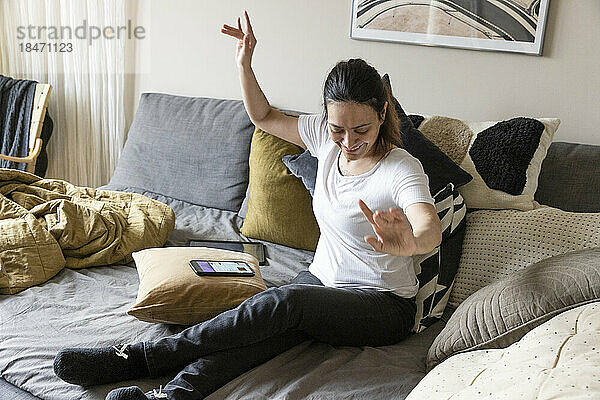 Unbeschwerte junge Frau mit Querschnittslähmung tanzt  während sie zu Hause auf dem Sofa sitzt