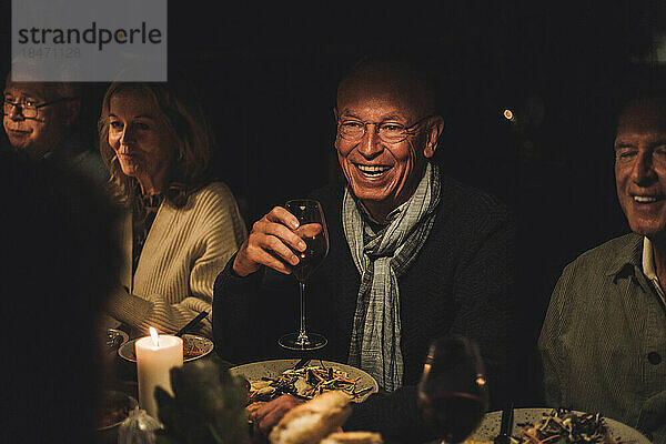Glücklicher älterer Mann mit Freunden während einer nächtlichen Dinnerparty