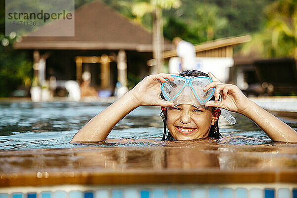 Porträt eines lächelnden Mädchens mit Schwimmbrille im Pool eines Ferienorts