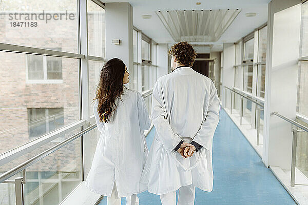 Rückansicht eines männlichen und eines weiblichen Arztes  die sich in einem Krankenhausflur unterhalten