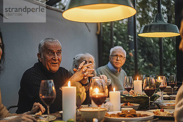 Reifer Mann mit verschränkten Händen  der mit männlichen und weiblichen Freunden auf einer Dinnerparty sitzt