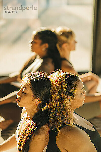 Freundinnen  die Rücken an Rücken sitzen und während einer Yogastunde üben