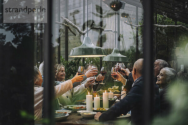 Glückliche ältere männliche und weibliche Freunde stoßen mit Wein während einer Dinnerparty im Hinterhof an