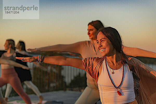 Glückliche Frau beim Yoga mit Freundin auf der Terrasse bei Sonnenuntergang