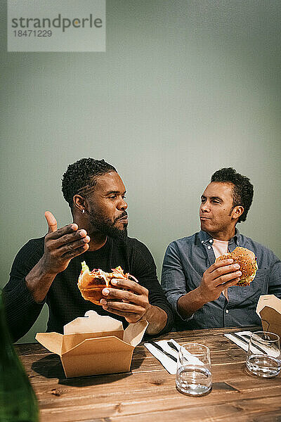 Männliche Freunde reden miteinander  während sie im Restaurant Burger essen