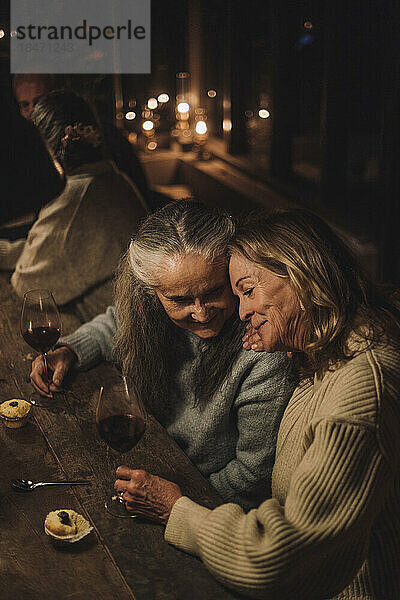 Lächelnde ältere weibliche Freunde mit Weingläsern  die während einer Party am Esstisch sitzen
