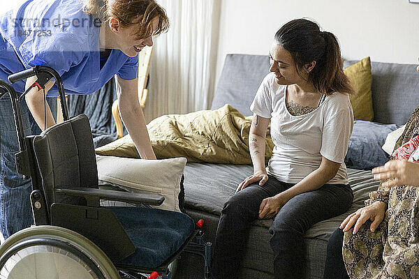 Krankenschwester stellt Rollstuhl für querschnittsgelähmte Frau ein  die zu Hause auf dem Sofa sitzt