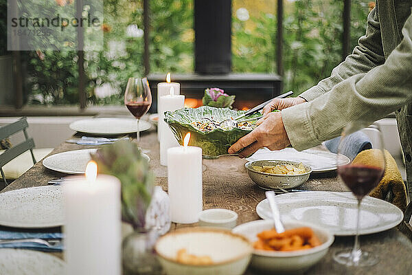 Hände eines älteren Mannes  der eine Salatschüssel hält  während er den Abendbrottisch für eine Party vorbereitet