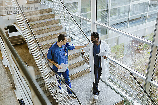 Hohe Winkel Ansicht der lächelnden männlichen Arzt und Krankenschwester diskutieren  während die Bewegung nach unten auf der Treppe im Krankenhaus
