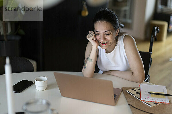 Glückliche Frau mit Querschnittslähmung genießt es  zu Hause den Laptop zu beobachten