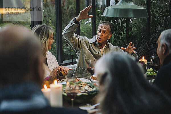 Älterer Mann gestikuliert beim Gespräch mit Freunden während einer Dinnerparty