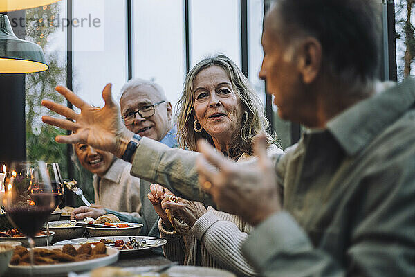Ältere Frau  die einem männlichen Freund zuhört  während sie auf einer Dinnerparty gestikuliert