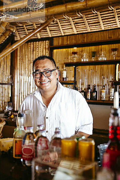 Porträt eines glücklichen Barkeepers mit Brille am Tresen in einem Ferienort