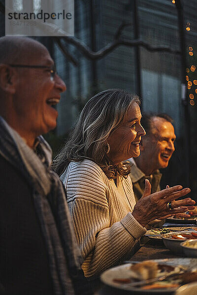 Glückliche ältere Frau gestikuliert beim Gespräch auf einer Dinnerparty