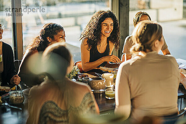 Junge Frau lacht mit Freundinnen beim Frühstück im Freizeitzentrum