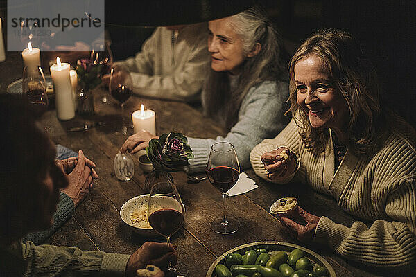 Lächelnde ältere Frau isst Muffin und unterhält sich mit einem Freund auf einer Party
