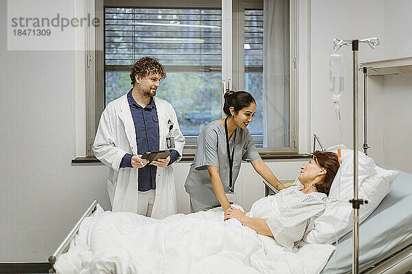 Lächelnde Krankenschwester im Gespräch mit einem älteren Patienten  der auf dem Bett eines Arztes im Krankenhaus liegt