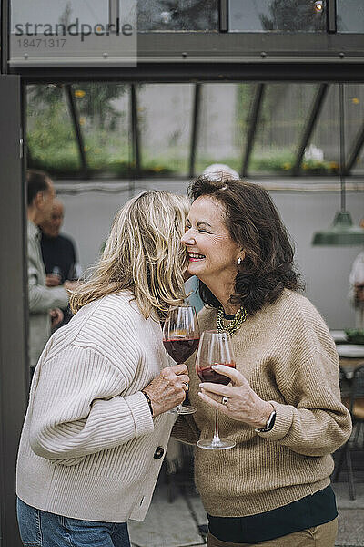 Glückliche Seniorinnen mit Weingläsern  die sich bei einer Dinnerparty begrüßen