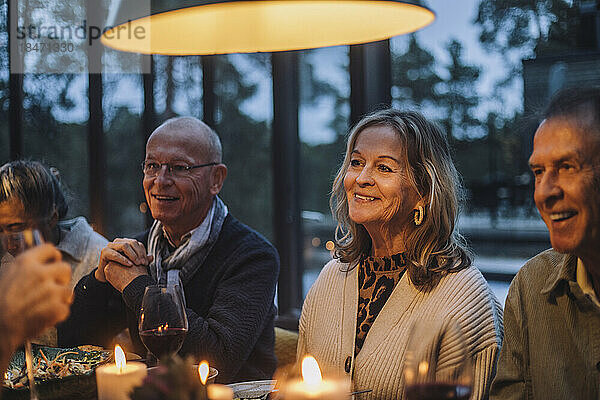 Lächelnde ältere Frau mit männlichen Freunden im Ruhestand während einer Dinnerparty