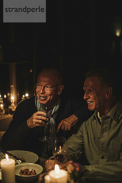 Glückliche ältere männliche Freunde genießen ein gemeinsames Abendessen bei Kerzenlicht auf einer Party