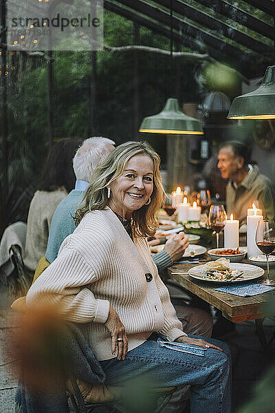 Seitenansicht Porträt einer lächelnden älteren Frau auf einem Stuhl sitzend während einer Dinnerparty