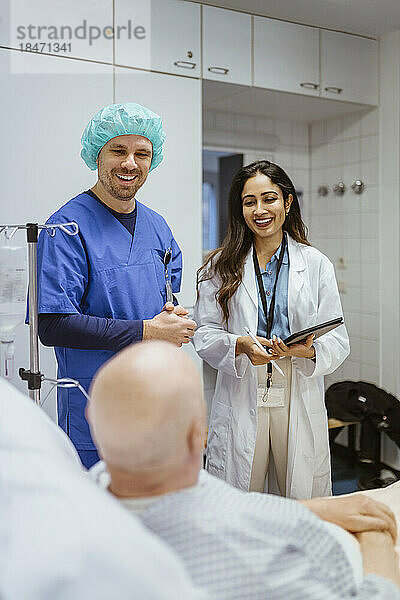 Fröhliches Gesundheitspersonal im Gespräch mit einem älteren männlichen Patienten im Krankenhaus