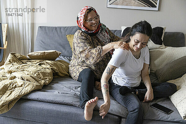 Glückliche Mutter massiert ihre querschnittsgelähmte Tochter  die zu Hause auf dem Sofa sitzt