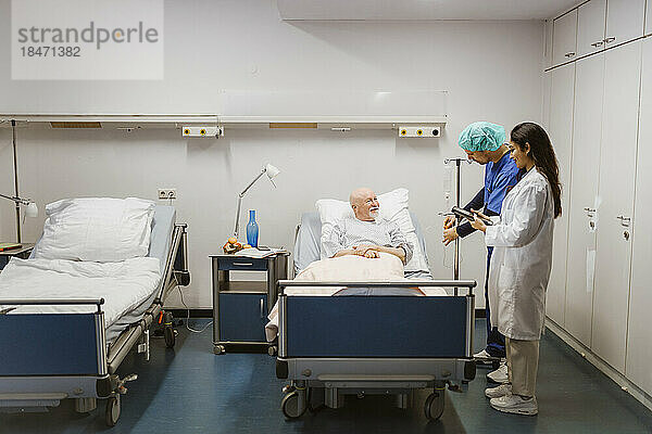 Lächelnder älterer männlicher Patient  der das Pflegepersonal im Krankenhaus ansieht