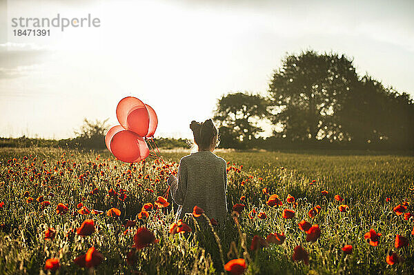 Mädchen läuft mit Luftballons inmitten von Mohnblumen