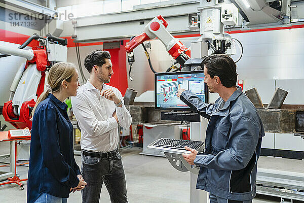 Kollegen schauen auf den Bildschirm  während sie mit einem Ingenieur in einer Roboterfabrik stehen