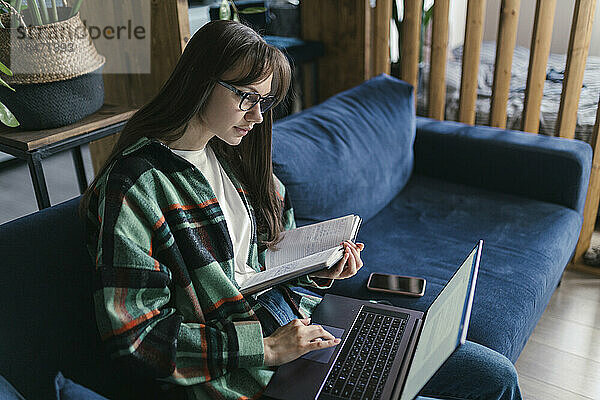 Junge Frau mit Buch und Laptop zu Hause