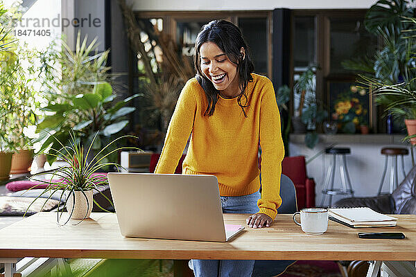 Glückliche Geschäftsfrau mit Laptop am Schreibtisch im Loft-Büro