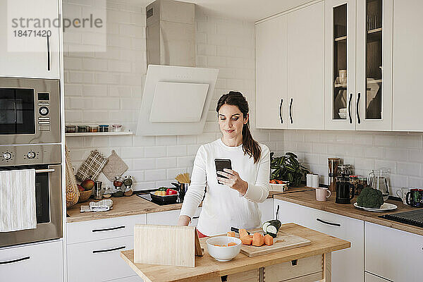 Lächelnde Frau benutzt Mobiltelefon in der heimischen Küche