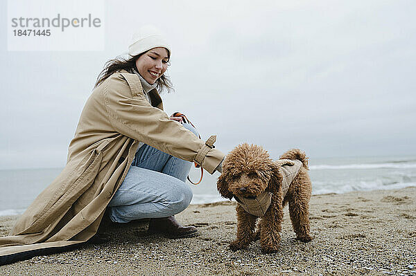 Lächelnde Frau streichelt Hund am Strand
