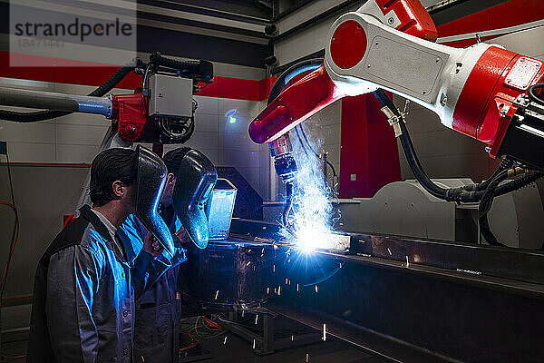 Ingenieure tragen Schutzkleidung beim Roboterarmschweißen in der Fabrik