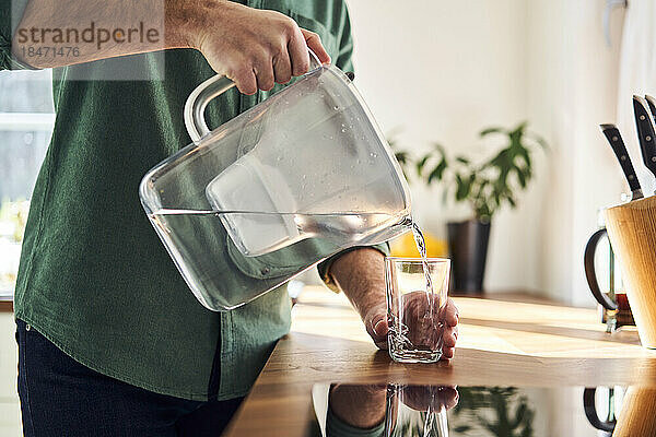 Mann gießt Wasser aus einer Filterkanne in ein Glas in der Küche  Nahaufnahme