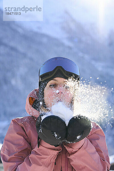 Frau mit Handschuhen bläst auf Schnee