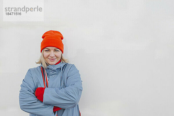 Lächelnde Frau mit verschränkten Armen vor weißer Wand